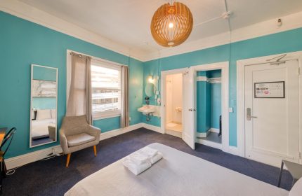HI San Francisco Downtown Hostel room. Gay-friendly hotel room featuring a bed, chair, and ensuite bathroom. Turquoise walls.