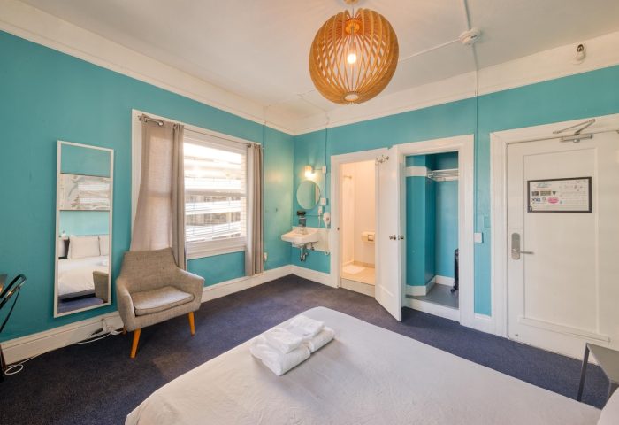 HI San Francisco Downtown Hostel room. Gay-friendly hotel room featuring a bed, chair, and ensuite bathroom. Turquoise walls.
