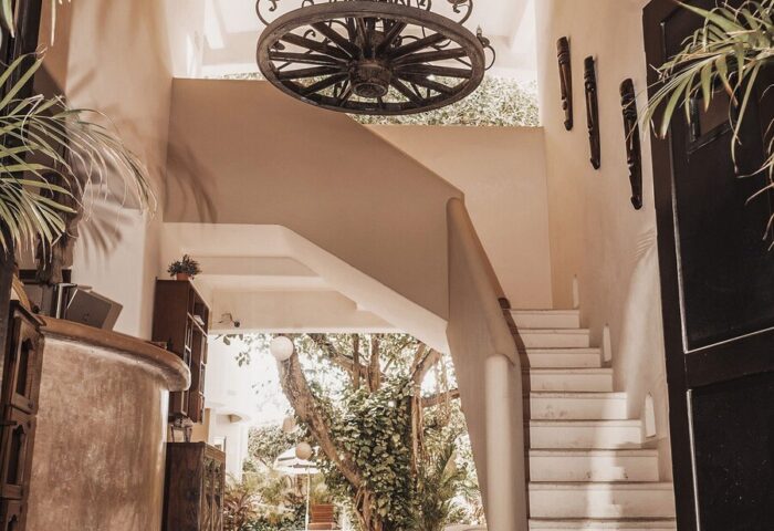 HOTEL POSADA 06 TULUM Adults Only interior. Staircase, chandelier, & plants. Gay-friendly hotel with unique design elements.