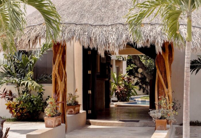 Hotel Posada 06 Tulum entrance. Adults-only, gay-friendly hotel with thatched roof, wooden pillars, and tropical plants. Pool view.