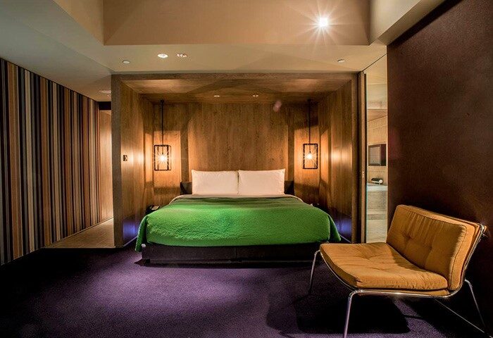HOTEL QUOTE Taipei room. Gay-friendly hotel room with wood paneling, green blanket, purple carpet, and a modern chair. Stylish Taipei lodging.
