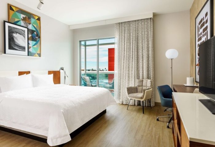 Hampton Inn & Suites Santa Monica guest room. Gay-friendly hotel with balcony, desk, and king bed. Modern decor, art, and comfortable seating.