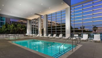Pool at Hampton Inn & Suites Santa Monica, a gay-friendly hotel. Lounge chairs line the pool deck with large windows.