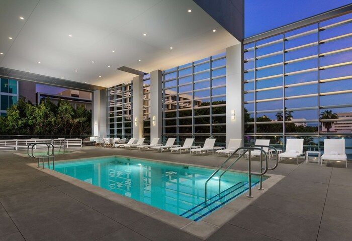 Pool at Hampton Inn & Suites Santa Monica, a gay-friendly hotel. Lounge chairs line the pool deck with large windows.