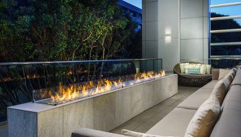 Outdoor lounge at Hampton Inn & Suites Santa Monica, a gay-friendly hotel. Features a modern fireplace, seating, and lush greenery.