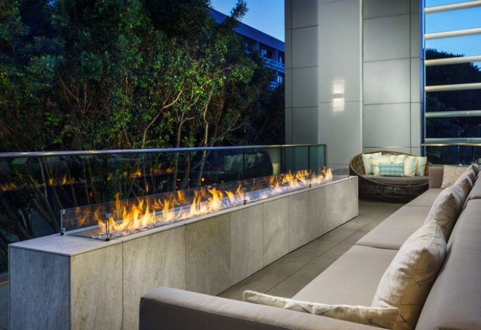 Outdoor lounge at Hampton Inn & Suites Santa Monica, a gay-friendly hotel. Features a modern fireplace, seating, and lush greenery.