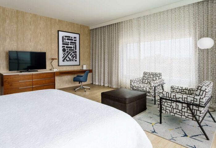 Hampton Inn & Suites Santa Monica room. Gay-friendly hotel with bed, TV, desk, chairs, and ottoman. Modern decor, comfortable for gay men travelers.