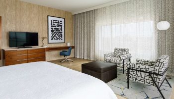 Hampton Inn & Suites Santa Monica room. Gay-friendly hotel with bed, TV, desk, chairs, and ottoman. Modern decor, comfortable for gay men travelers.