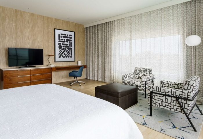 Hampton Inn & Suites Santa Monica room. Gay-friendly hotel with bed, TV, desk, chairs, and ottoman. Modern decor, comfortable for gay men travelers.