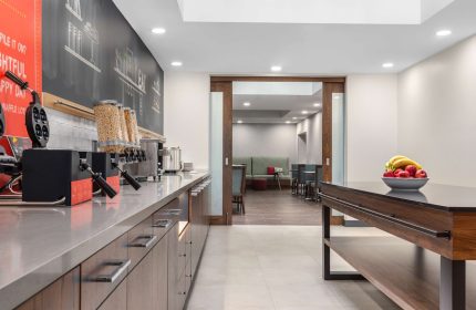 Breakfast area at Hampton Inn & Suites by Hilton Toronto Downtown, a gay-friendly hotel. Waffle maker, cereal, fruit, and seating visible.