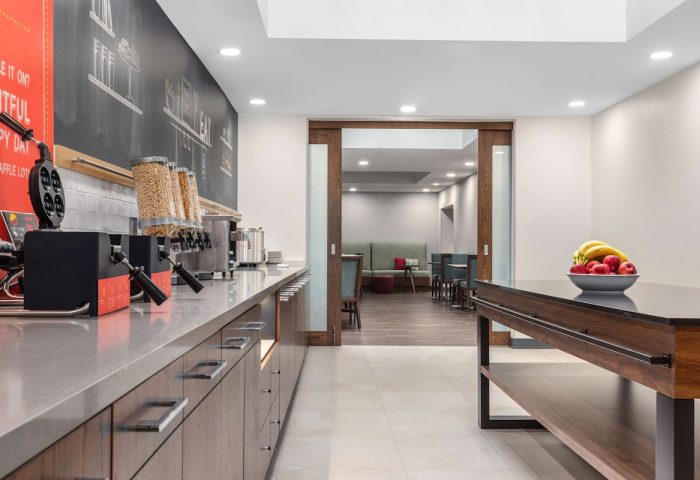 Breakfast area at Hampton Inn & Suites by Hilton Toronto Downtown, a gay-friendly hotel. Waffle maker, cereal, fruit, and seating visible.