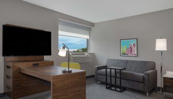 Hampton Inn & Suites by Hilton Toronto Downtown guest room. Desk, TV, sofa, and window. Gay-friendly hotel for gay men travelers.