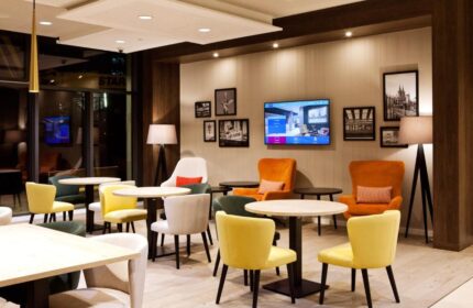 Lounge area at Hampton by Hilton Berlin City East Side Gallery, a gay-friendly, pet-friendly hotel. Tables, chairs, and a TV create a welcoming space.