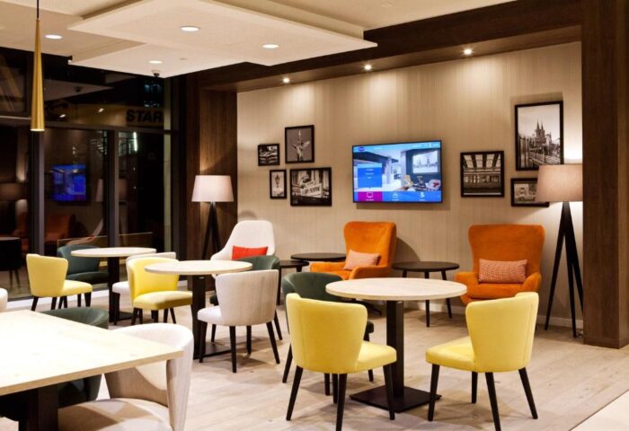 Lounge area at Hampton by Hilton Berlin City East Side Gallery, a gay-friendly, pet-friendly hotel. Tables, chairs, and a TV create a welcoming space.