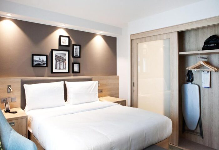 Hampton by Hilton Berlin City East Side Gallery's bedroom. Pet-friendly, gay-friendly hotel room with bed, closet, iron, and hairdryer.