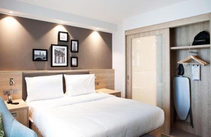 Hampton by Hilton Berlin City East Side Gallery's bedroom. Pet-friendly, gay-friendly hotel room with bed, closet, iron, and hairdryer.
