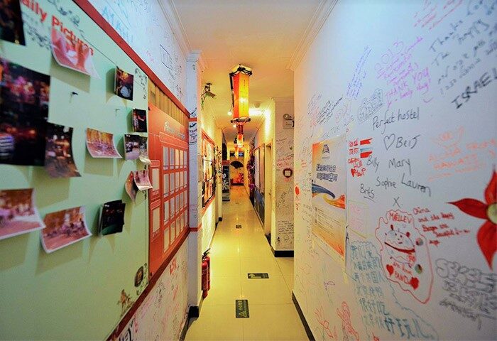 Hallway view at Happy Dragon Backpackers Hostel, a gay-friendly hotel. Walls covered in photos and guest signatures. Lanterns hang from the ceiling.