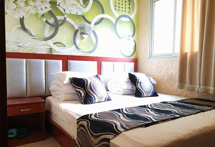 Happy Dragon Backpackers Hostel room. Gay-friendly hotel bedroom with bed, pillows, bedside table, and decorative wallpaper. Gay travel.