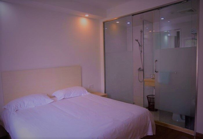 Harcourts Kailun Hotel room. Gay-friendly hotel featuring a double bed with white linens and a modern glass-enclosed bathroom with shower.