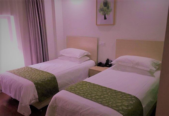 Harcourts Kailun Hotel room. Two twin beds with white linens and green accents. Gay-friendly hotel room with simple decor. Travel advice.