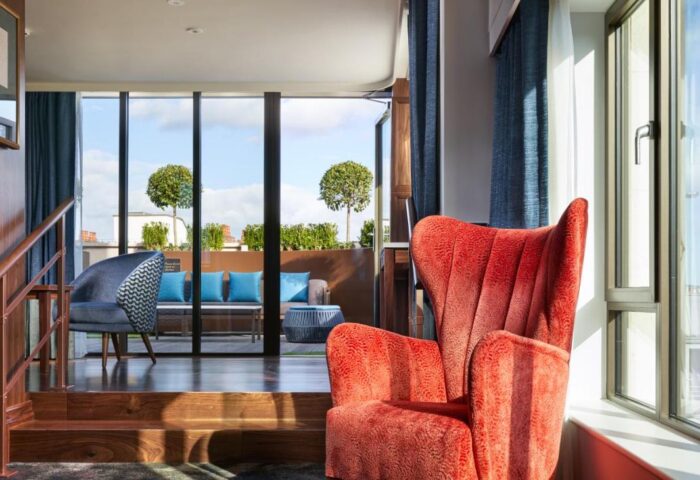 Hard Rock Hotel Dublin's gay-friendly room. Red armchair near the window. Balcony view with outdoor seating. Modern, stylish design.