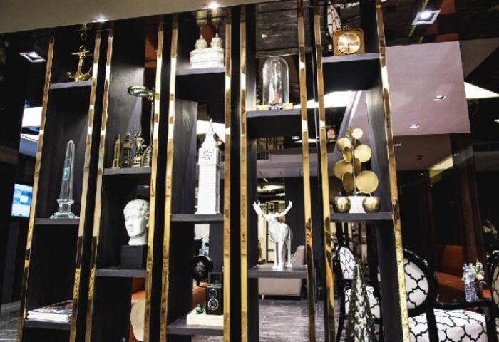 Haven't Met Silom gay-friendly hotel decor. Shelves with gold accents display decorative objects: clock, deer statue, camera, and bust.