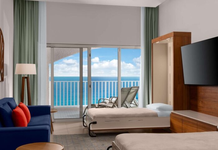 Hilton Cancun Mar Caribe All-Inclusive Resort room. Ocean view from balcony. Gay-friendly hotel with modern decor, sofa, and Murphy beds.