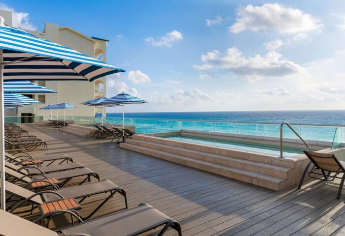 Hilton Cancun Mar Caribe All-Inclusive Resort pool deck. Gay-friendly hotel with ocean view, lounge chairs, and blue striped umbrellas.