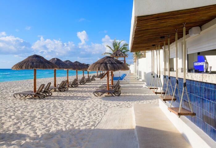 Beachfront view at Hilton Cancun Mar Caribe All-Inclusive Resort, a gay-friendly hotel. Lounge chairs, umbrellas, and a bar with swings.