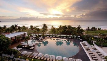 Hilton Phuket Arcadia Resort & Spa pool view at sunset. Gay-friendly hotel with beach access and palm trees. Ideal for gay travel.