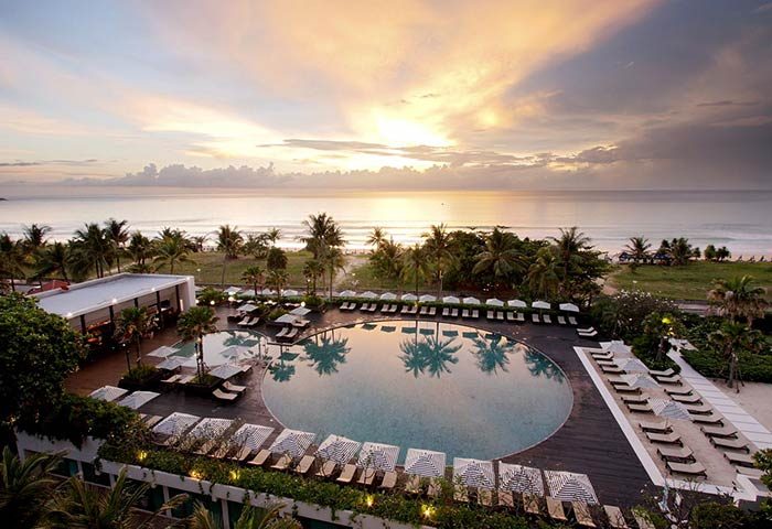 Hilton Phuket Arcadia Resort & Spa pool view at sunset. Gay-friendly hotel with beach access and palm trees. Ideal for gay travel.