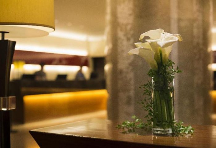 Hilton Tokyo detail: vase of calla lilies on a wooden table. Lamp, reception area in background. Gay-friendly hotel, elegant, welcoming.