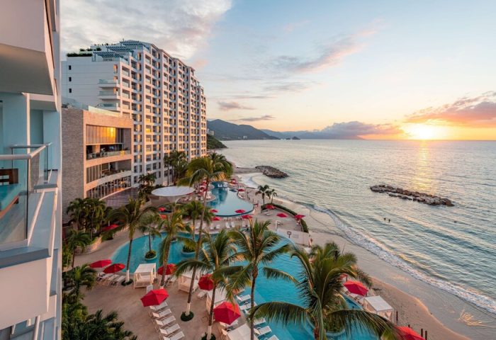 Hilton Vallarta Riviera All-Inclusive Resort, a gay-friendly hotel. Ocean view with pools, palm trees, and beach at sunset.