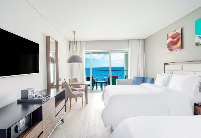 Hilton Vallarta Riviera All-Inclusive Resort room. Gay-friendly hotel with ocean view, balcony, two beds, dining table, and modern decor. Perfect for gay travel.