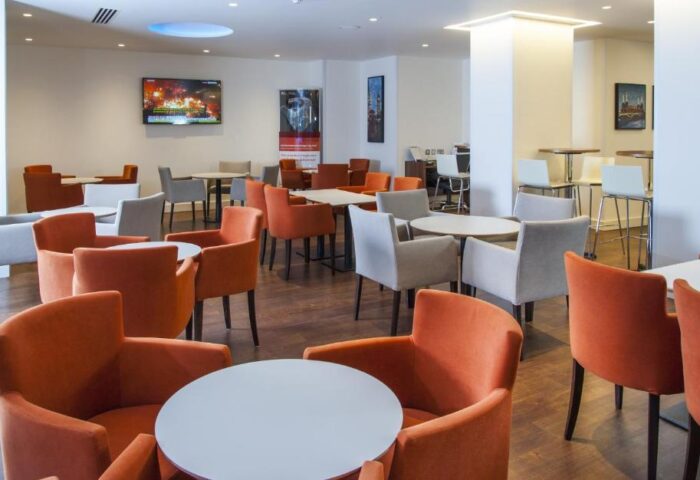 Holiday Inn Express London Vauxhall Nine Elms's lounge area. Round tables, orange and gray chairs, TV. Gay-friendly hotel interior.
