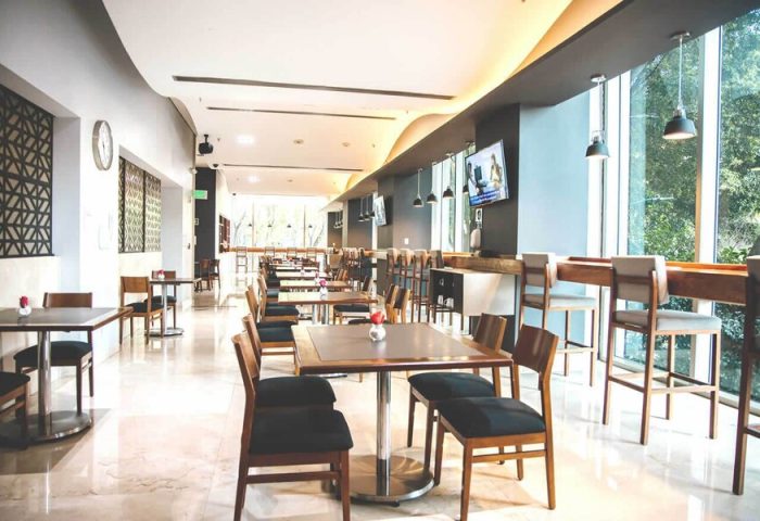 Holiday Inn Express Mexico Reforma gay-friendly hotel restaurant. Tables and chairs in a bright, modern dining area. Bar seating by large windows.