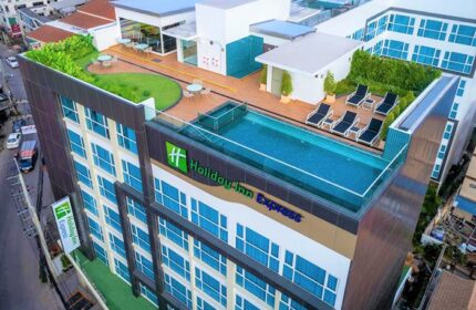 Holiday Inn Express Pattaya Central, a gay-friendly hotel. Rooftop pool, lounge chairs, tables, and greenery. Modern architecture with blue windows.