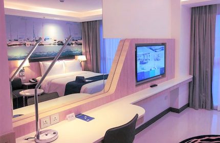 Holiday Inn Express Pattaya Central gay-friendly hotel room. Features a bed, desk, TV, and a mural of boats on the wall. Modern design.