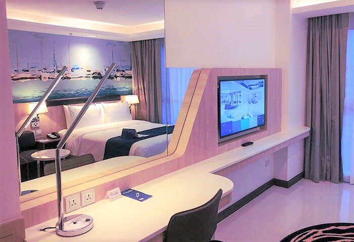 Holiday Inn Express Pattaya Central gay-friendly hotel room. Features a bed, desk, TV, and a mural of boats on the wall. Modern design.