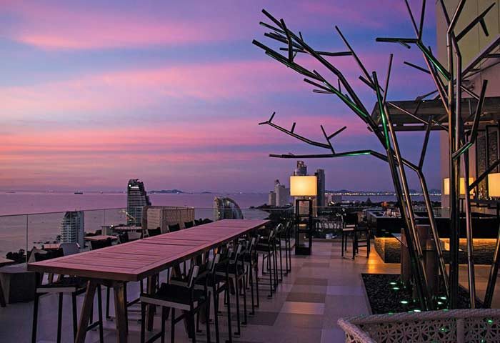 Holiday Inn Pattaya rooftop bar at sunset. Gay-friendly hotel with ocean view, tables, and decorative tree. Pattaya, Thailand.