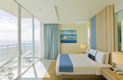 Holiday Inn Pattaya gay-friendly hotel room. Balcony with ocean view, lounge chairs. Modern design, blue accents. Ideal for gay travel in Thailand.