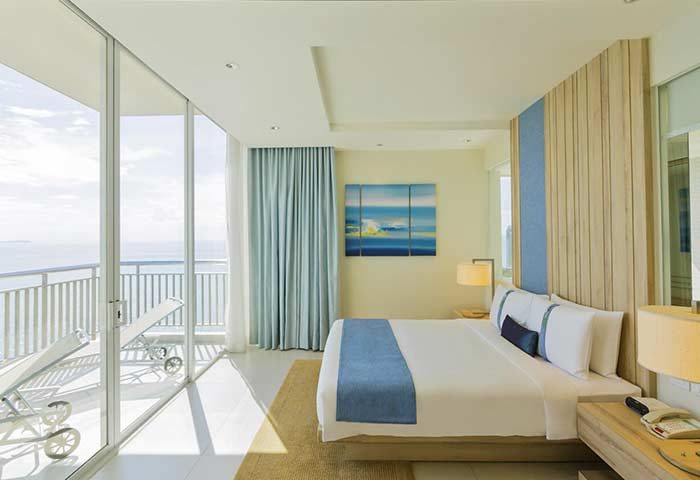 Holiday Inn Pattaya gay-friendly hotel room. Balcony with ocean view, lounge chairs. Modern design, blue accents. Ideal for gay travel in Thailand.