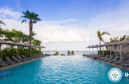 Holiday Inn Pattaya gay-friendly hotel infinity pool view. Tropical trees, sun loungers, and umbrellas by the pool overlooking the ocean.