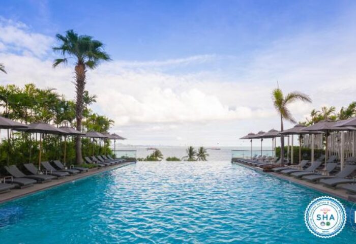 Holiday Inn Pattaya gay-friendly hotel infinity pool view. Tropical trees, sun loungers, and umbrellas by the pool overlooking the ocean.