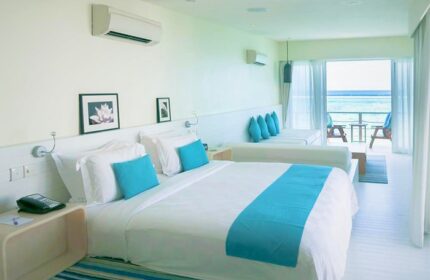 Holiday Inn Resort Kandooma Maldives gay-friendly hotel room. White bedding with turquoise accents, balcony with ocean view, seating area.