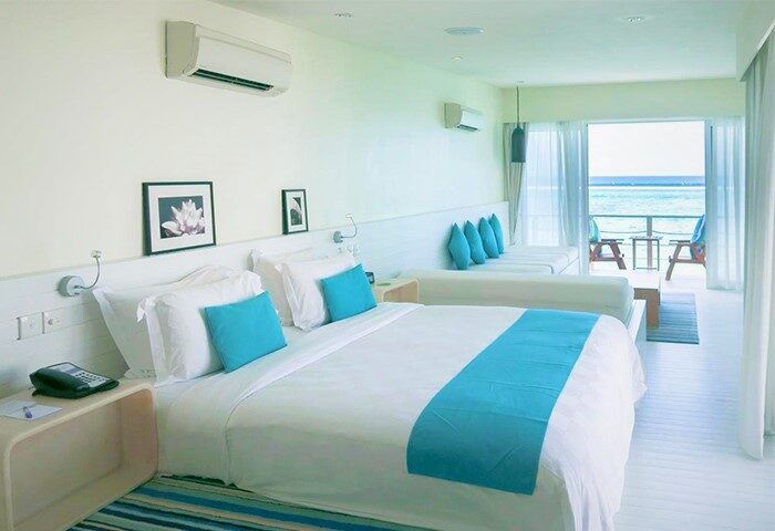 Holiday Inn Resort Kandooma Maldives gay-friendly hotel room. White bedding with turquoise accents, balcony with ocean view, seating area.