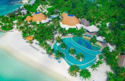 Aerial view of Holiday Inn Resort Kandooma Maldives, a gay-friendly hotel. Palm trees, beach, pool, and thatched-roof buildings.