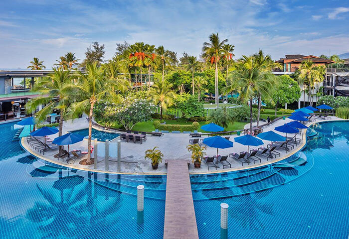 Holiday Inn Resort Krabi Ao Nang Beach pool view. Gay-friendly hotel with palm trees, blue umbrellas, and lounge chairs. Tropical paradise.