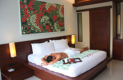 Holiday Inn Resort Krabi Ao Nang Beach gay-friendly hotel room. Man relaxing on bed with fruit tray. Modern decor, luxury travel.