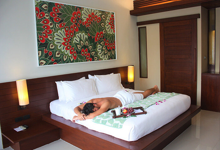 Holiday Inn Resort Krabi Ao Nang Beach gay-friendly hotel room. Man relaxing on bed with fruit tray. Modern decor, luxury travel.